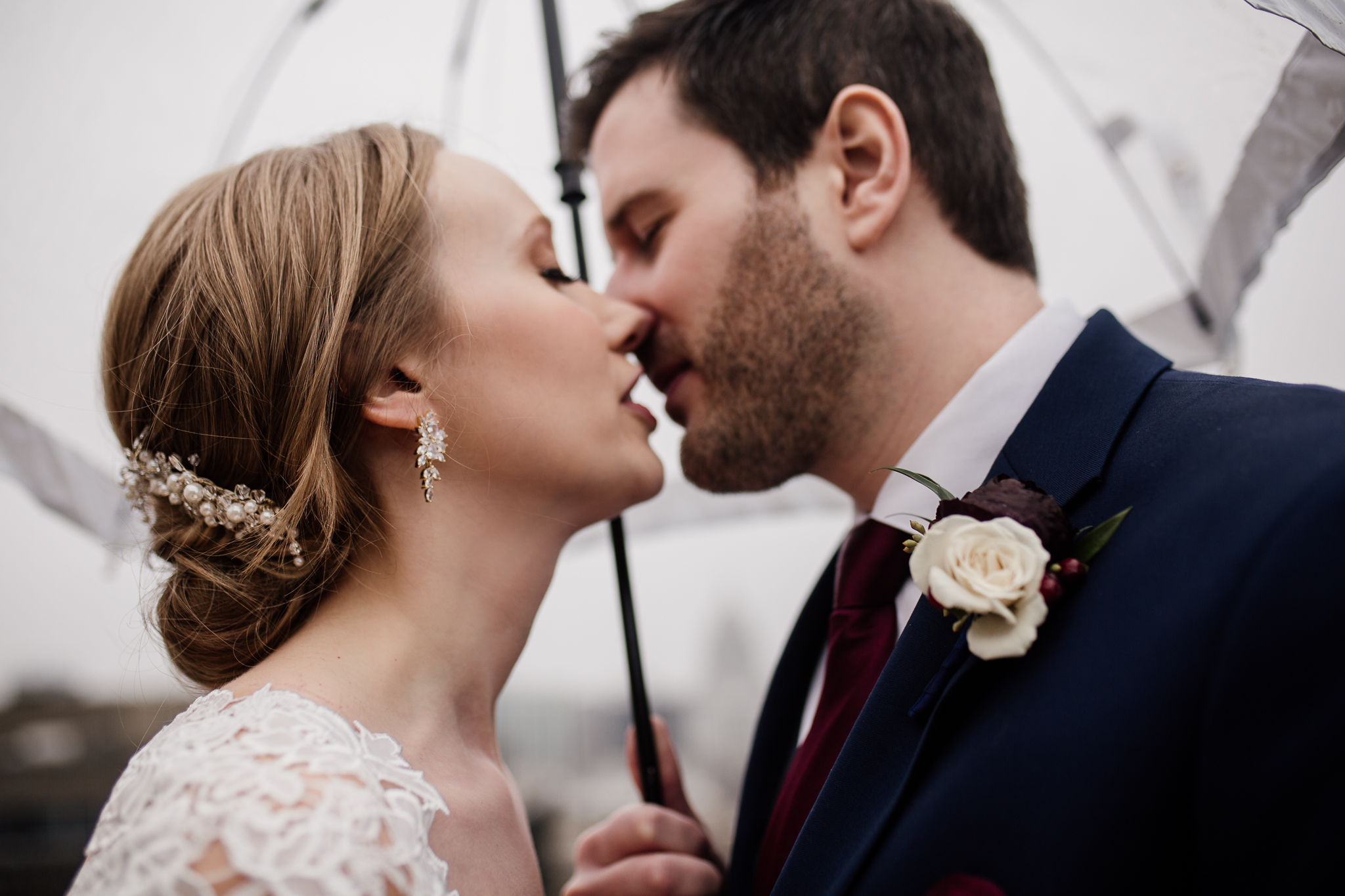 Madison Wedding Photographer's portrait of bride and groom kissing under an umbrella in the rain on the Edgewater Hotel rooftoop.